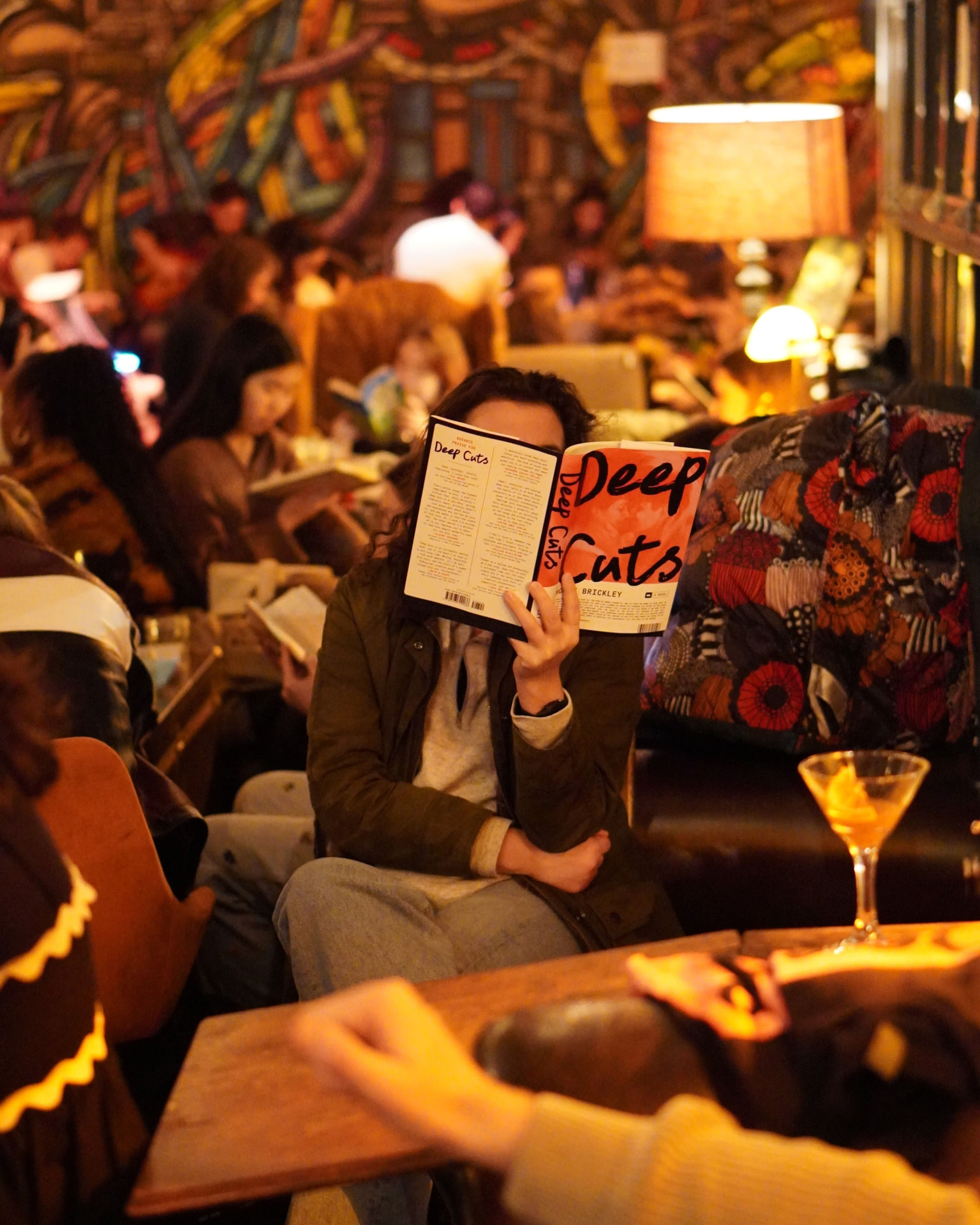 Une personne lit un roman dans un bar chaleureux, un cocktail posé sur la table